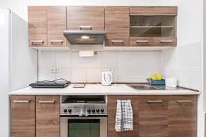 A kitchen with wooden cabinets, a built-in oven, a stove, a kettle, and a sink. - Holiday Apartment “SaarGlück” with Mountain Views and Wi-Fi (Beckingen)