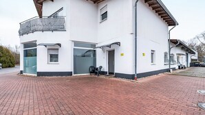 A two-story building with a balcony, a garage, and a paved driveway. - Holiday Apartment “SaarGlück” with Mountain Views and Wi-Fi (Beckingen)