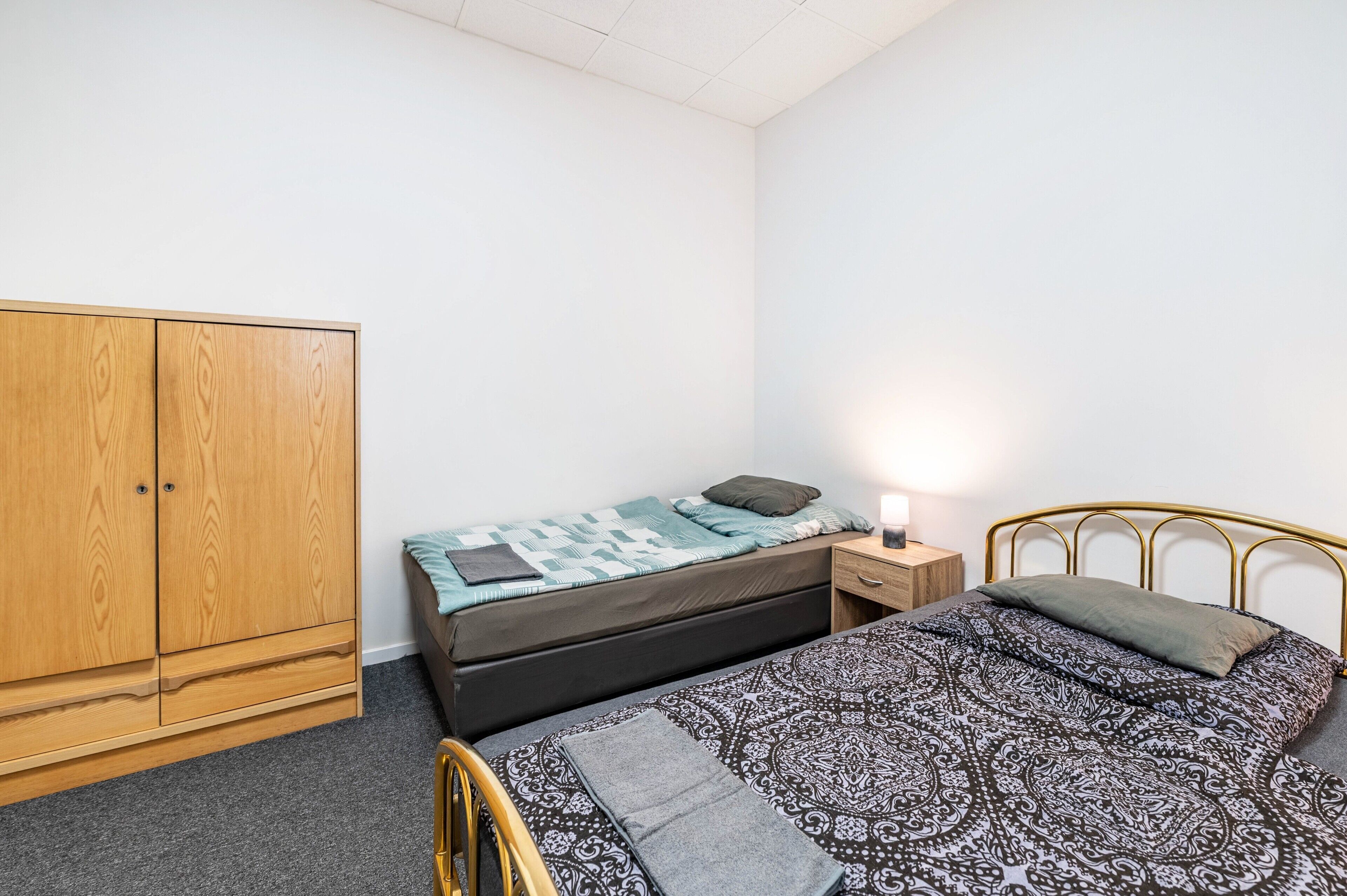 A bedroom with a bed, a wardrobe, a bedside table, and a lamp.