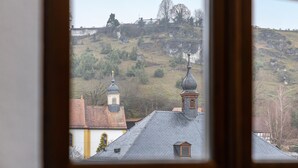 Uitzicht door een raam op een gebouw, met een kerktoren en een heuvel met schaarse begroeiing.