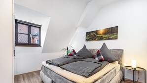 Een slaapkamer met een bed, een raam, een schilderij en een nachtkastje met een lamp.
