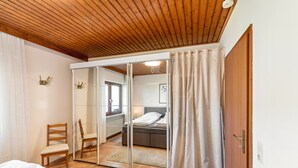 A bedroom with a wooden ceiling, a sliding glass door leading to a bathroom, a bed, a chair, and a bedside table. - Wanderbar Apartment on the Rhine with Private Terrace, Garden, and Wi-Fi (Kamp-Bornhofen)