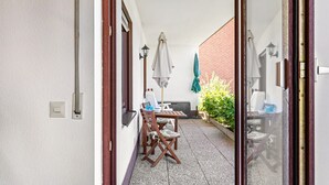 A patio with a table and chairs, a green umbrella, and a brick wall. - Wanderbar Apartment on the Rhine with Private Terrace, Garden, and Wi-Fi (Kamp-Bornhofen)