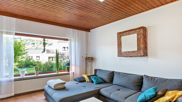 A modern living room with a grey sectional sofa, a glass coffee table, and a view of greenery outside. - Wanderbar Apartment on the Rhine with Private Terrace, Garden, and Wi-Fi (Kamp-Bornhofen)