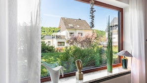 A window with a view of a residential area, a white vase, a green vase, and a lamp on the windowsill. - Wanderbar Apartment on the Rhine with Private Terrace, Garden, and Wi-Fi (Kamp-Bornhofen)