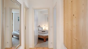 Een gang die leidt naar een slaapkamer met een bed, nachtkastje en een lamp.