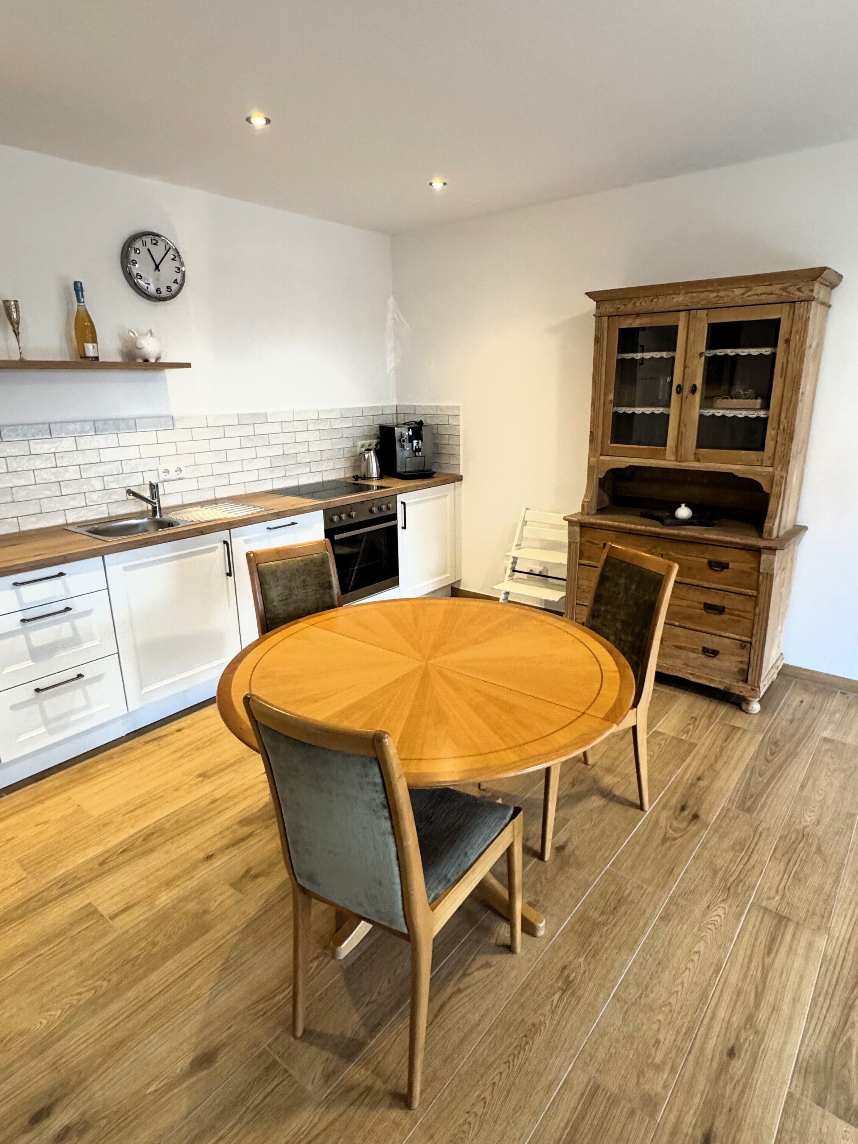 A kitchen with a round wooden table, chairs, a coffee machine, and a cabinet.
