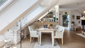 Ett loftliknande vardagsrum med matplats, kök och ett stort fönster.