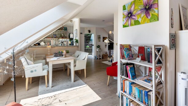 En modern loftlägenhet med ett matområde, en bokhylla och en trappa som leder upp till ett övre plan.