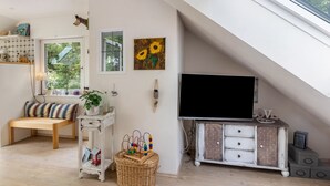 Ett mysigt rum med ett sluttande tak, en träbänk, en tv, en korg av rotting och en hylla som är monterad på väggen.