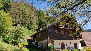 A traditional chalet with a stone foundation, wooden balconies, and a garden with flowering plants.
