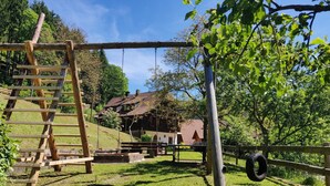 Un ensemble de balançoires en bois, une balançoire faite d’un pneu et une maison rustique avec un toit en pente.