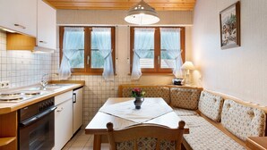 Une cuisine avec des meubles de rangement en bois, une cuisinière, un évier et un coin repas comprenant une table et un banc.