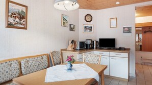 A cozy room with a wooden ceiling, a dining table with a vase of flowers, a kitchen area with a coffee maker, and a television.