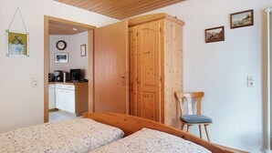 Une chambre avec deux lits, une armoire en bois, une chaise, un petit coin cuisine et une table à manger.
