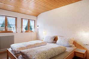 A bedroom with two beds, a wooden ceiling, a radiator, and a window with curtains.
