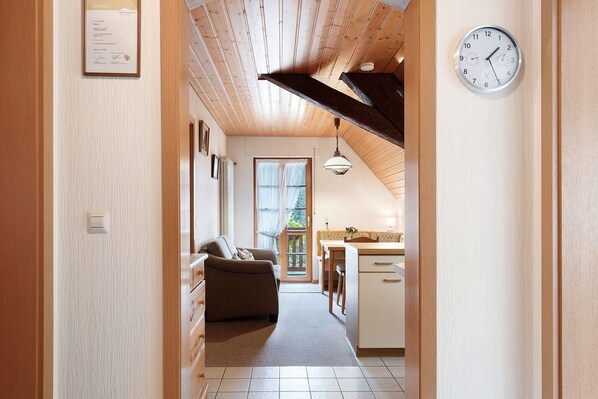 Un pasillo estrecho que da a una sala de estar con sofá, una mesa de comedor y una cocina con pileta y placares.