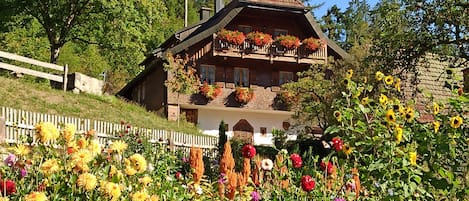 A chalet with a sloped roof, wooden balconies, and a garden with various flowers.