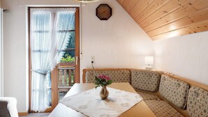 A cozy room with a wooden ceiling, a clock on the wall, a table with a vase of flowers, and a bench with patterned cushions.