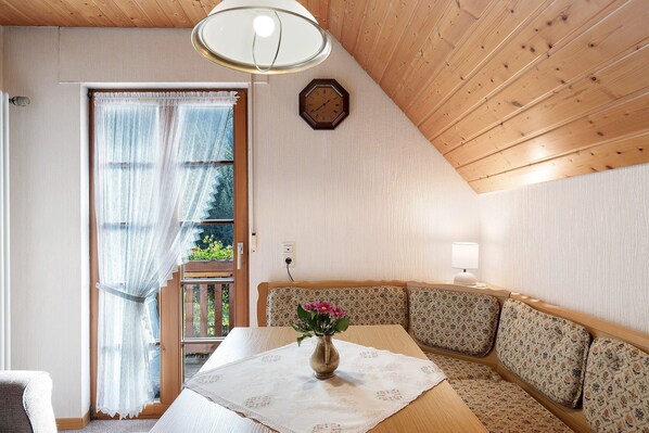 Una habitación acogedora con techo de madera, un reloj en la pared, una mesa con un florero y un banco con cojines estampados.