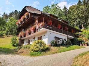 A traditional wooden chalet with balconies adorned with flowers, set in a lush, green valley.