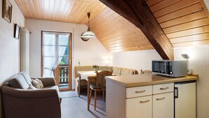 A cozy room with a wooden ceiling, a dining table with chairs, a sofa, and a kitchenette with a microwave.