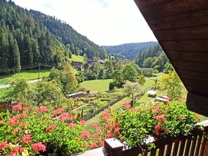 A balcony with a view of a green valley, houses, and a forested hillside.