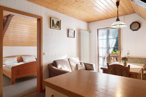 A cozy room with a wooden ceiling, a bed, a sofa, a dining table, and a window with curtains.