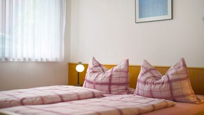 Ein Schlafzimmer mit zwei Betten, einer Nachttischlampe, einem Fenster mit Jalousien und einem gerahmten Bild an der Wand.