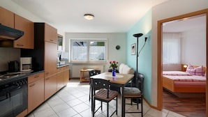 Eine kompakte Küche mit modernen Geräten, ein Essbereich mit Tisch und Stühlen sowie ein Schlafzimmer mit Bett und Vorhängen.