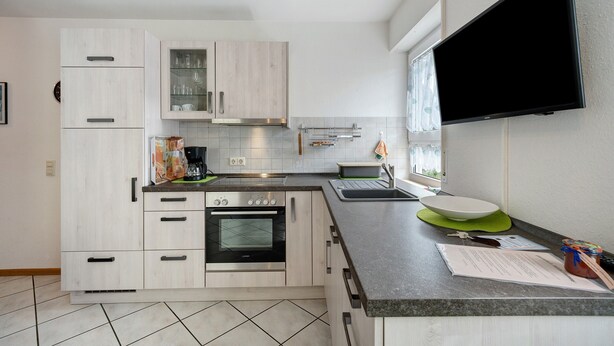 A modern kitchen with white cabinetry, a built-in oven, a large flat-screen TV mounted on the wall, and a window providing natural light. - Apartment '2' with Private Terrace and Wi-Fi in Endingen (Endingen)