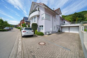 Ein zweigeschossiges Wohngebäude mit gepflasterter Auffahrt, einem weißen Auto auf der Straße und blauem Himmel.