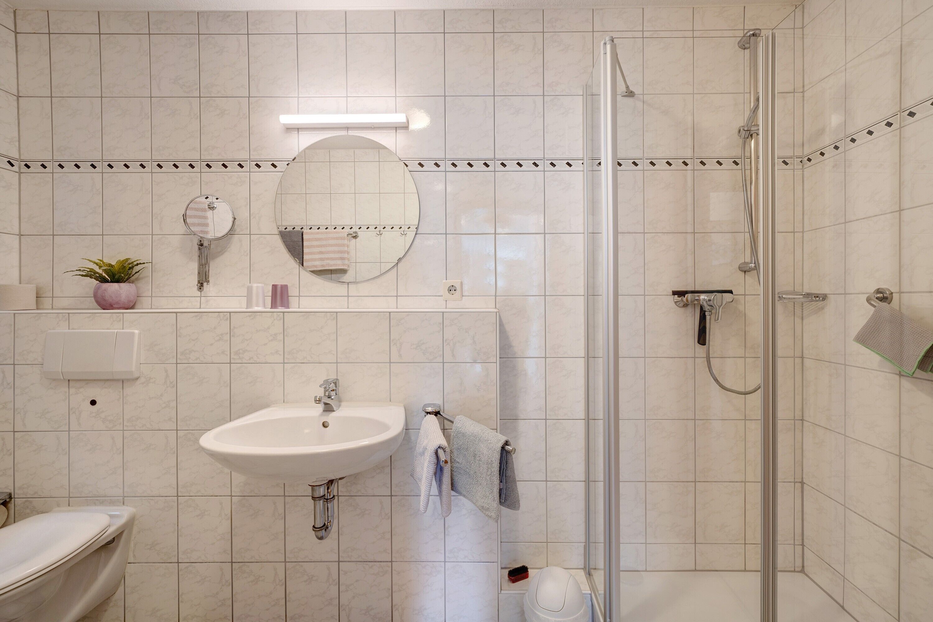 Une salle de bain équipée d’un lavabo, d’un miroir, d’un porte-serviettes, d’une douche et de toilettes.
