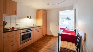 A modern kitchen with wooden cabinets, a built-in oven, and a dining area with a red table and chairs.