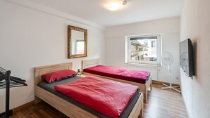 A bedroom with two beds, a mirror, a window, and a fan.