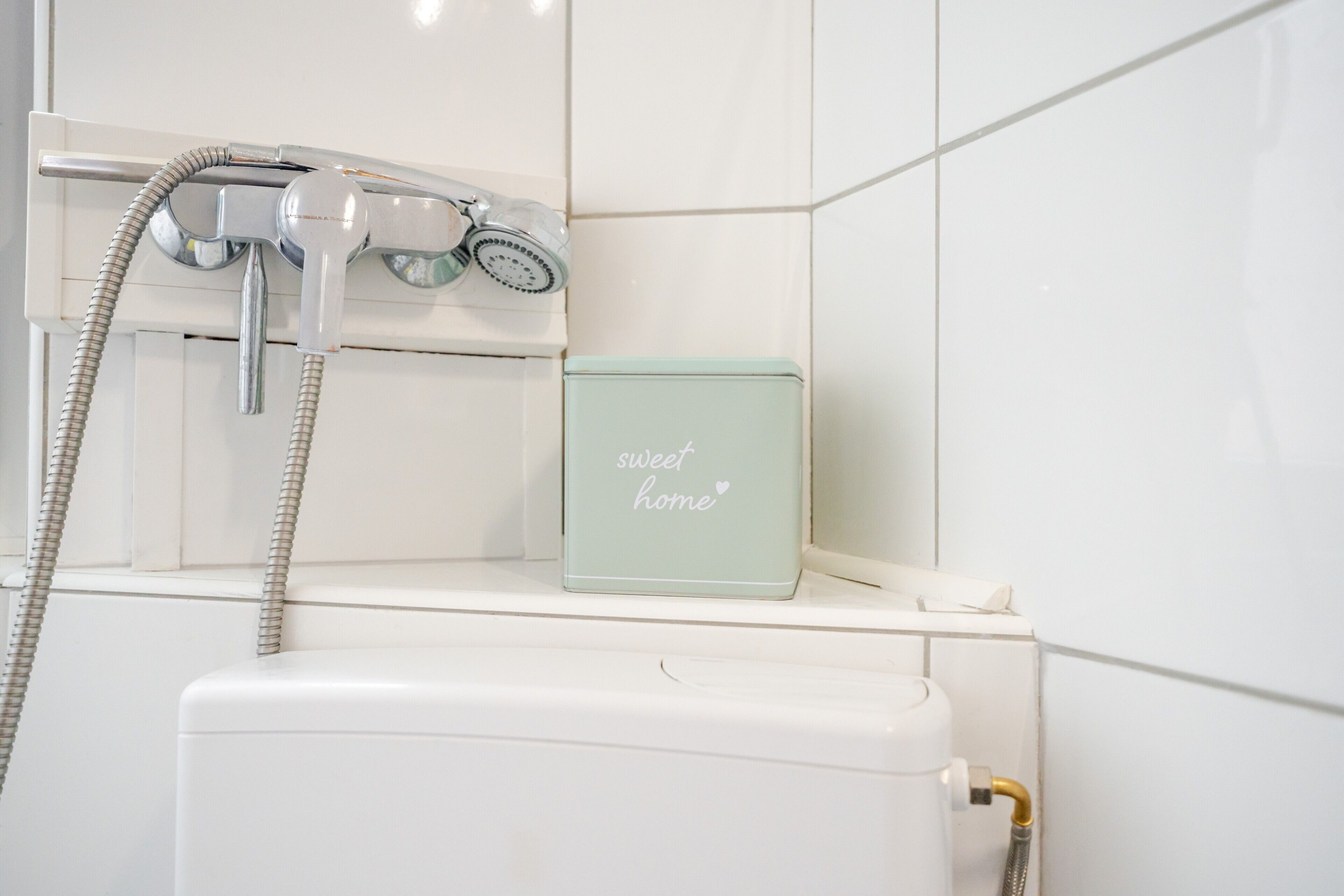 Ein Badezimmer mit Dusche, Toilette und einem Regal mit einer Box, auf der 'sweet home' steht.