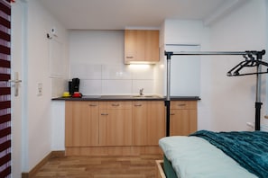 Ein kleines Zimmer mit einer Küchenzeile, einem Bett und einem Fenster.
