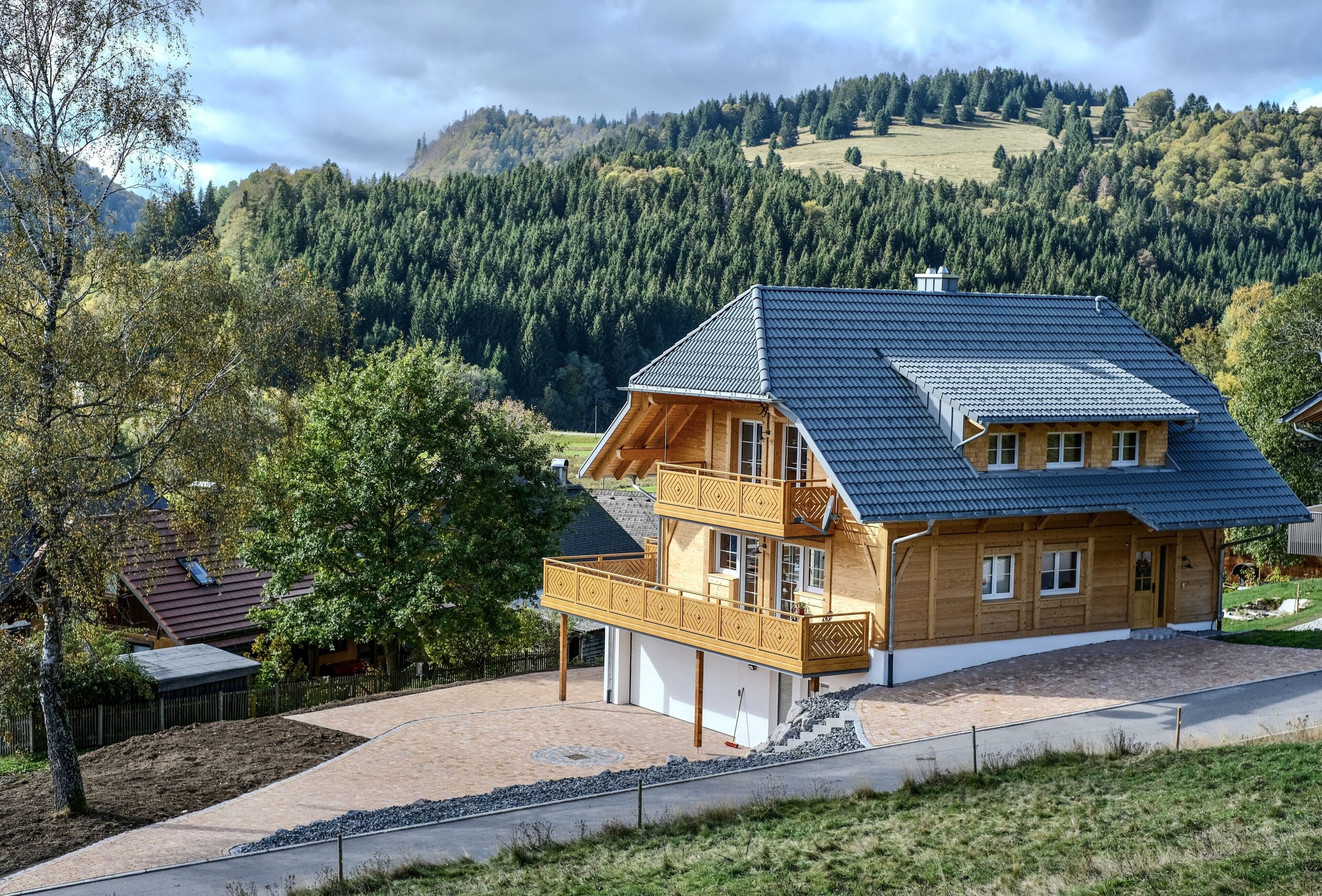 Ein zweistöckiges Holzhaus mit Balkon, Garage und Auffahrt zu einer Straße.