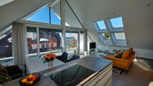 A modern living room with a large skylight, a dining area with a kitchen island, and a view of a building across the street.