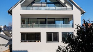 A modern two-story house with a flat roof, large windows, and a balcony.