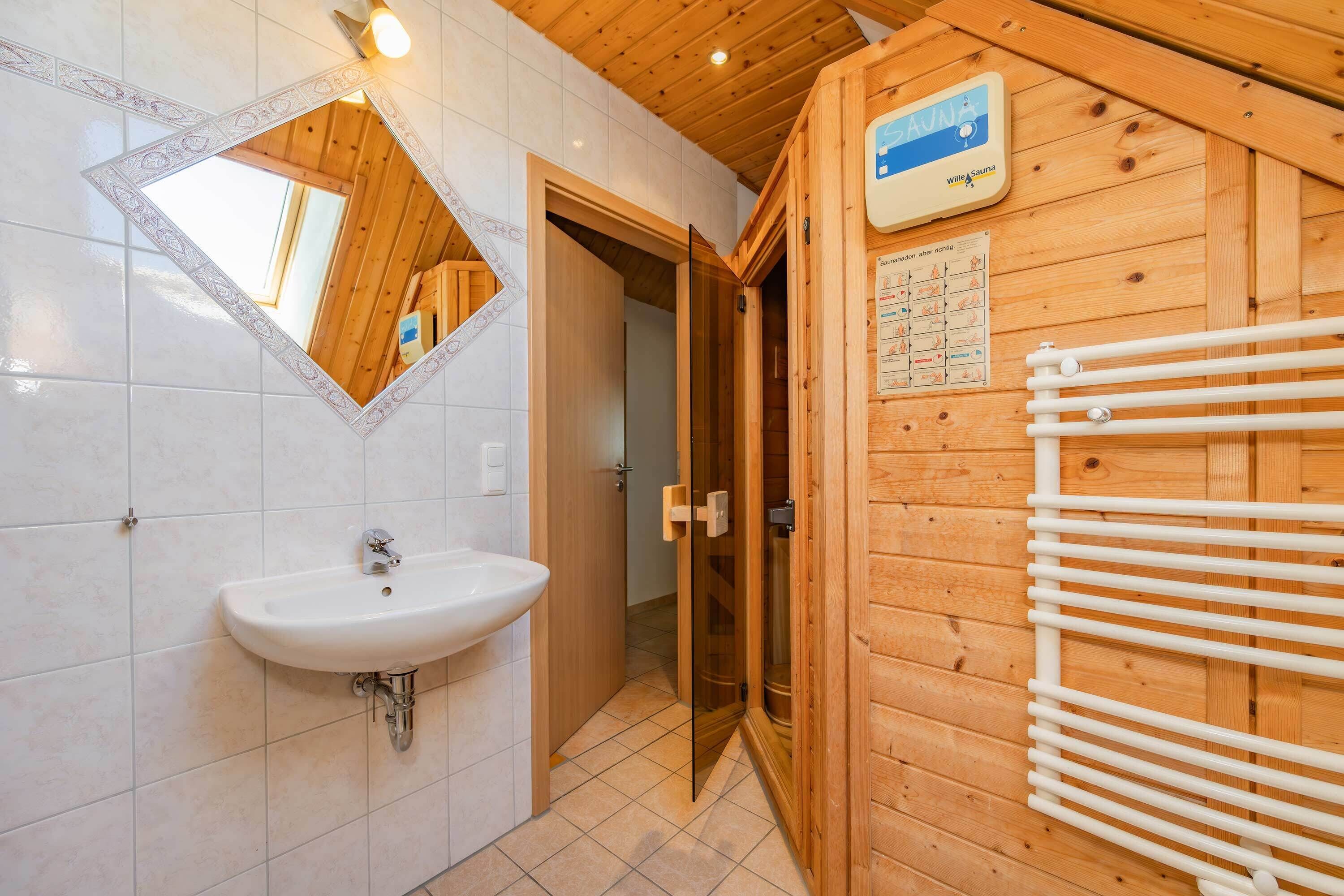 Een houten badkamer in een chalet, met een witte wastafel, een spiegel met decoratieve lijst en een bordje voor de sauna.