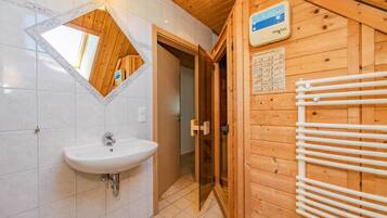 Een houten badkamer in een chalet, met een witte wastafel, een spiegel met decoratieve lijst en een bordje voor de sauna.