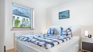 A bedroom with a bed, a window, a bedside table, and a wall-mounted picture.