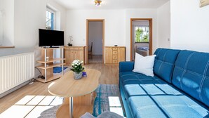 A modern living room with a television, wooden furniture, a blue sofa, and a view through a door.