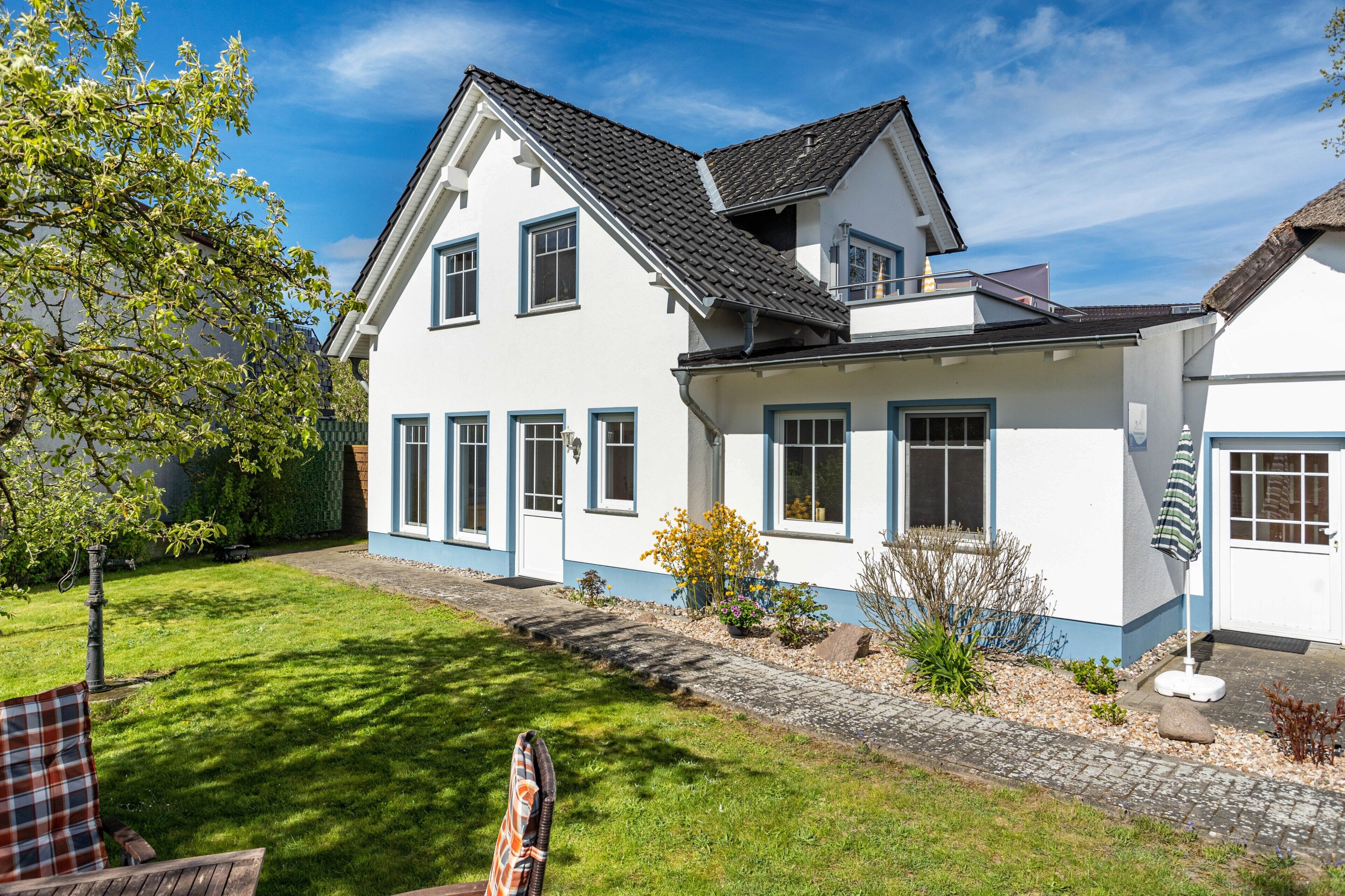 Et toetagers hus med en belagt indkørsel, græsplæne og en have med forskellige planter og blomster.