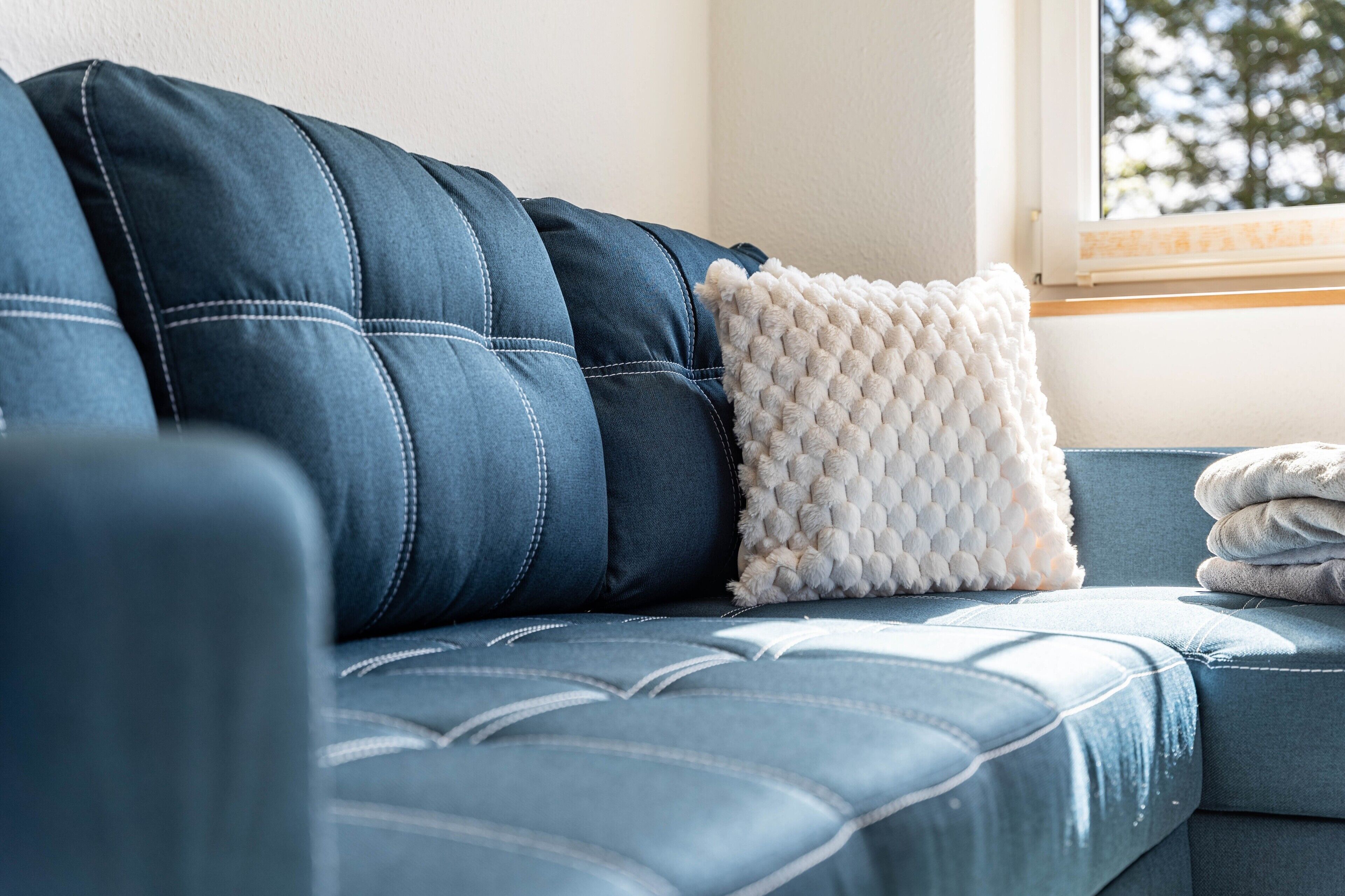 Ein blaues Sofa mit einem weißen, strukturierten Kissen und einer zusammengefalteten Decke.