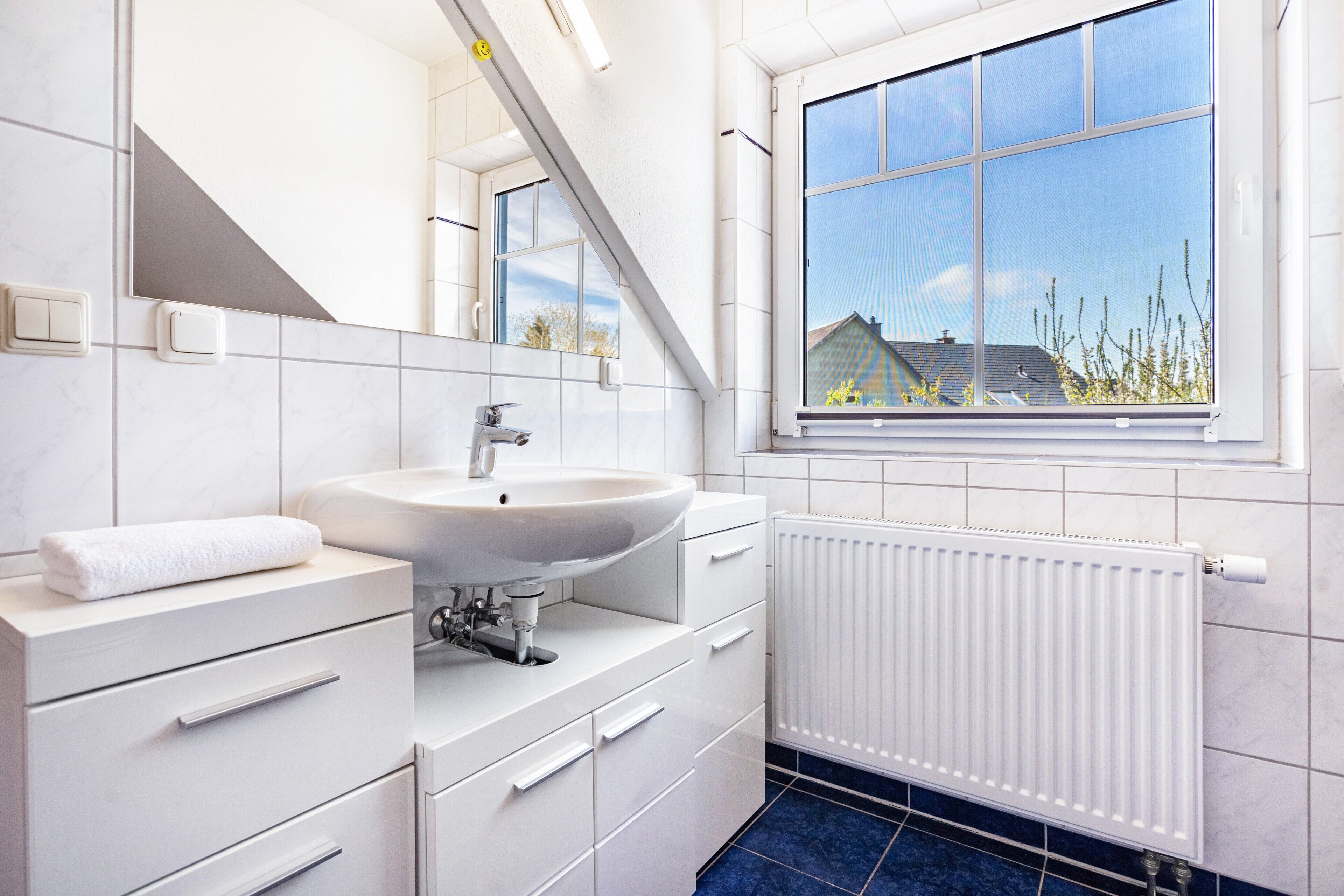 A modern bathroom with a white sink, mirror, and white cabinetry.