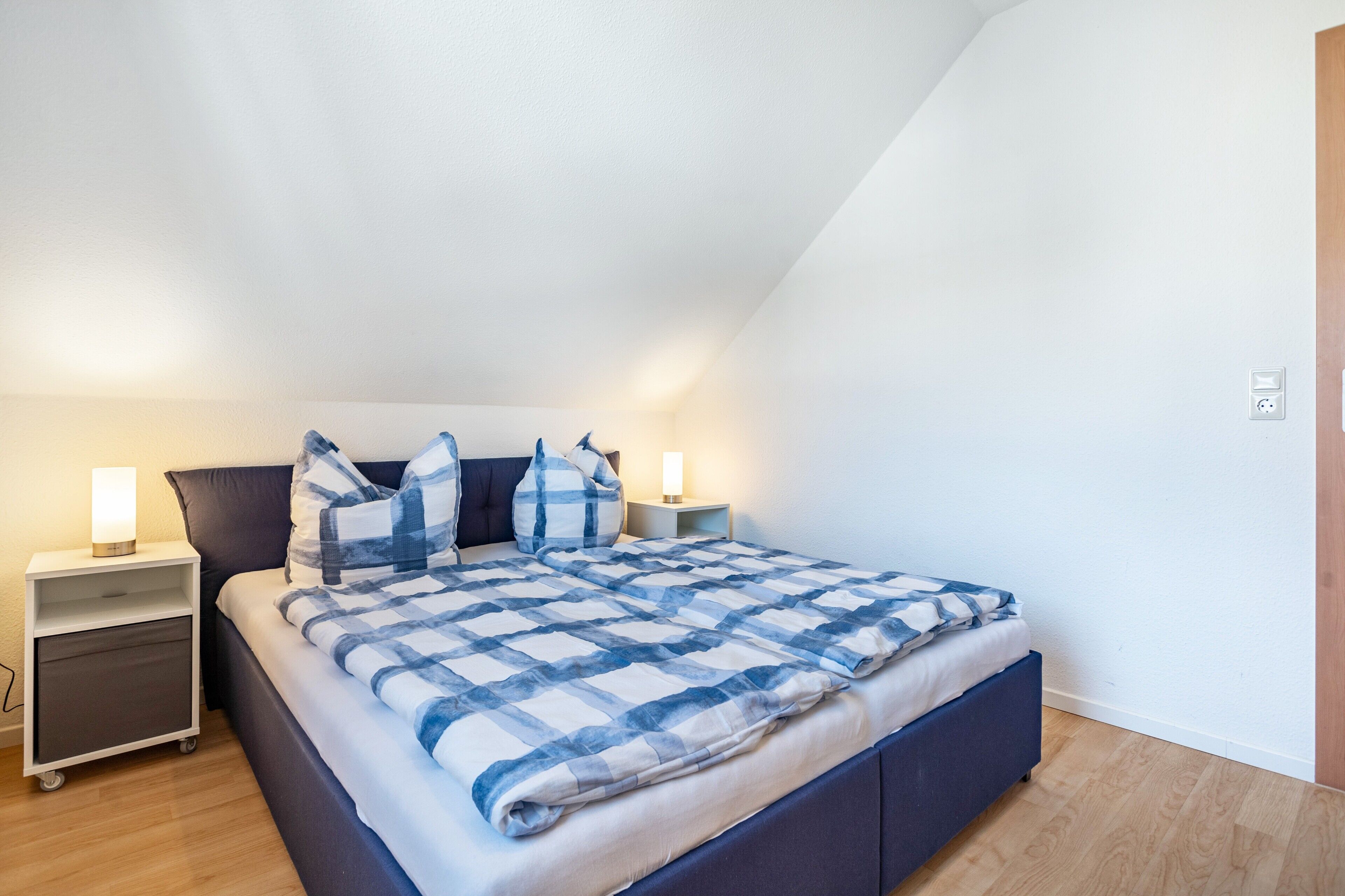 A bedroom with a bed, nightstands, and a wall socket.