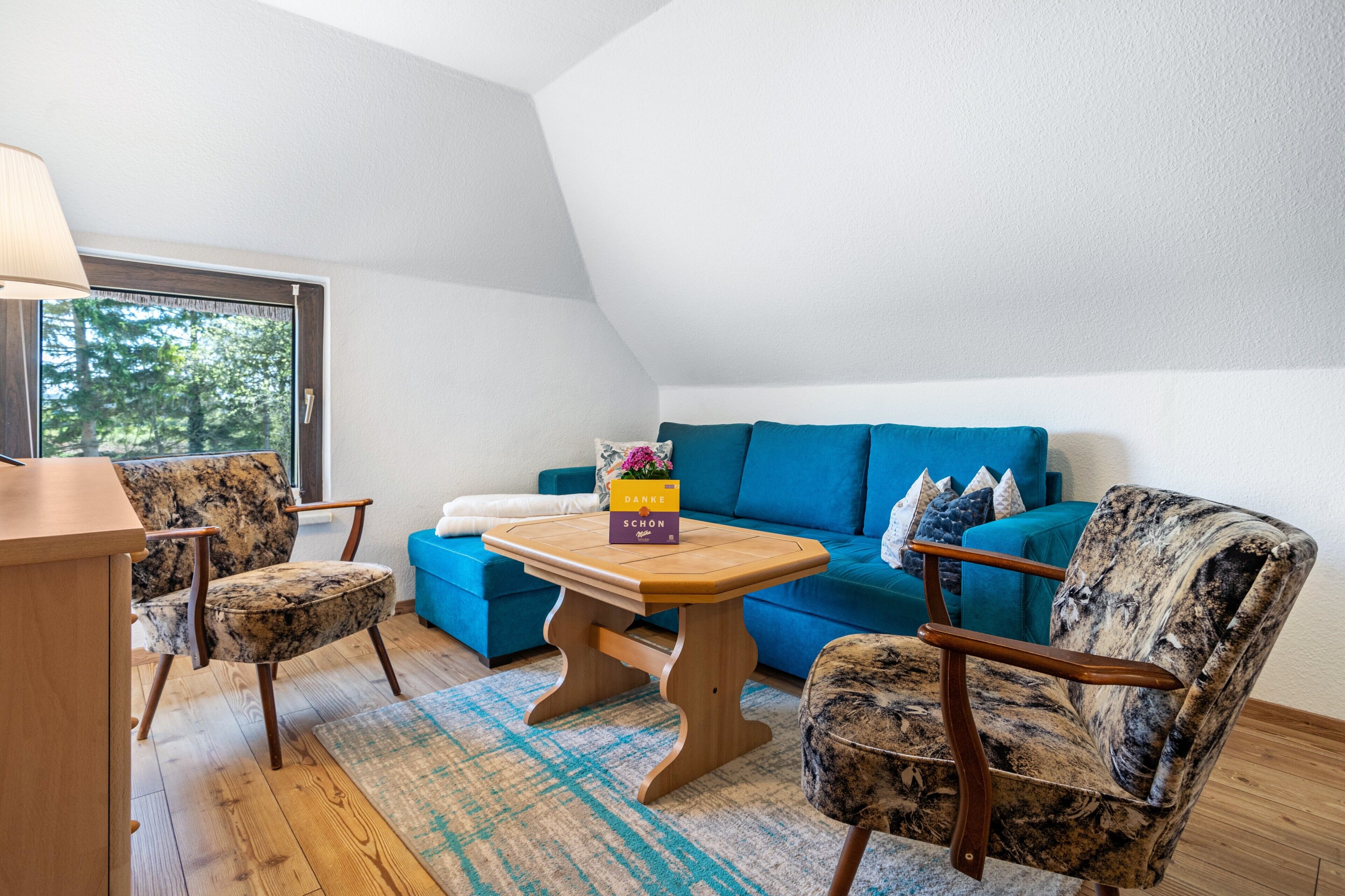 Ein Zimmer mit einem blauen Sofa, einem Holztisch und einem gemusterten Sessel.