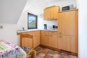 A small kitchen with wooden cabinets, a microwave, a coffee maker, and a window with a view of a house.